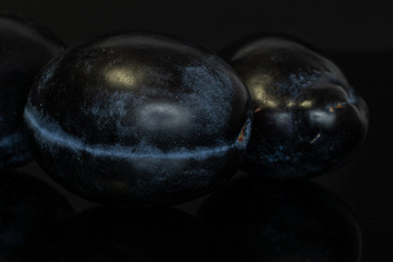 Group of two whole fresh purple plum isolated on black glass