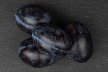 Group of four whole fresh purple plum flatlay on grey stone