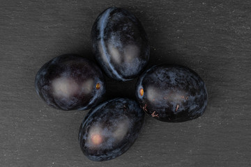 Group of four whole fresh purple plum flatlay on grey stone