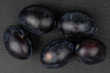 Group of five whole fresh purple plum flatlay on grey stone