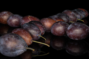 Lot of whole crossed sweet purple plum isolated on black glass