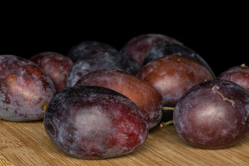 Lot of whole sweet purple plum on bamboo cutting board isolated on black glass