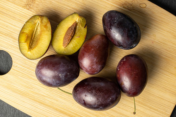 Fototapeta premium Group of five whole two halves of sweet purple plum on bamboo cutting board flatlay on grey stone
