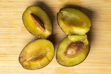Group of four halves of sweet purple plum flatlay on light wood