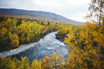 Sunny fall autumn view of Abisko National Park, Kiruna Municipality, Lapland, Norrbotten County, Sweden, with Abiskojokk river, road and Nuolja mountain, near border of Finland, Sweden and Norway