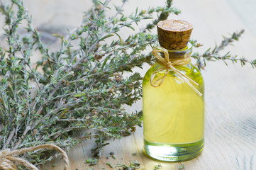 glass bottle of thyme essential oil and bunch of dry thyme on wooden rustic background. Dried spice...