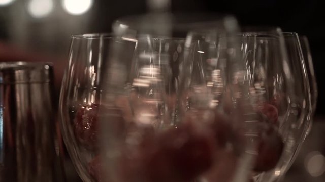 Large grapes in cold champagne glasses at a fancy restaurant, close-up. Skillful barman making alcoholic cocktails with fresh fruits in transparent glasses on bar counter under soft evening lighting.