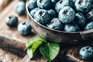 Freshly picked blueberries in bowl on wooden background. Healthy eating and nutrition.