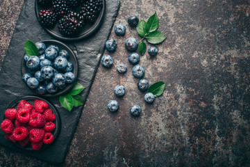 Fresh berries with raspberries, blueberries, blackberries in bowl on a stone stand on a dark metal background.