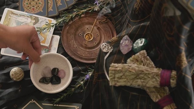 Altar with sage, tarot cards, burning incense and a hand placing crystals