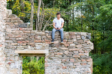 Young man with cell phone on wall of abandoned building
