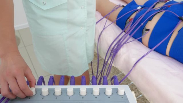 the girl lies on the couch and receives the procedure of myostimulation on her legs and buttocks in a beauty salon. Body care, weight loss.