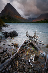 Naklejka premium The wind moving the water at Swiftcurrent Lake, with the sunrise lighting up the mountains in the background, Montana.