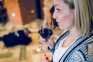 Young blonde woman holding a glass of red vine at home or the restaurant smelling before taste at the party