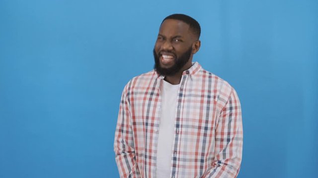 black african american man smiling sarcastically at camera, closeup. Isolated blue background. 4K