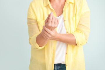 Mature woman suffering from pain in wrist on light background