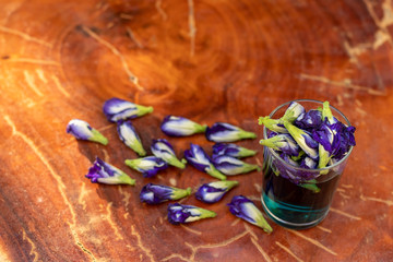 Purple butterfly pea flowers in a glass on a wooden floor.