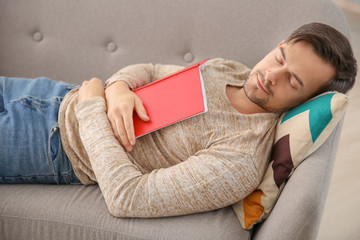 Handsome man with book sleeping on sofa at home
