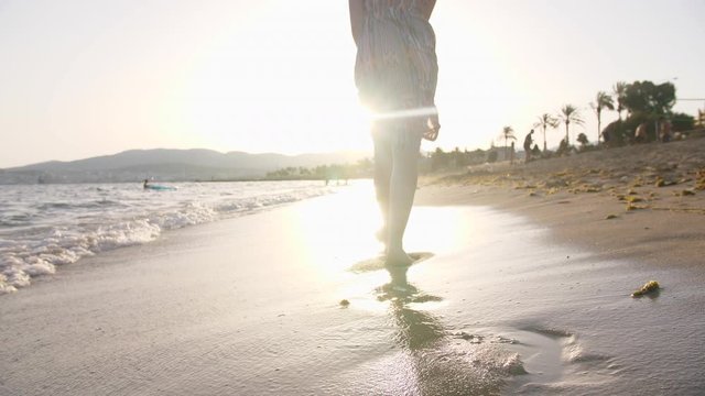 Footsteps on Sandy Beach with Sea Waves on Coast. Young Woman   Walking Along Seaside Shore with Sunset Water Surf in Spain..