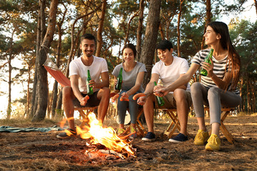 Young friends roasting sausages on fire and drinking beer at camp