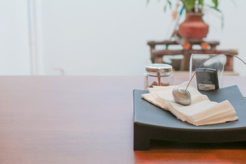 Metal paperweight on stack of white square paper napkin. modern paper napkin holder Close up napkin holder with paperweight to keep brown napkins on black plate and wooden table in coffee shop