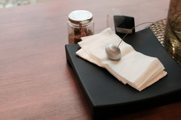 Metal paperweight on stack of white square paper napkin. modern paper napkin holder Close up napkin holder with paperweight to keep brown napkins on black plate and wooden table in coffee shop