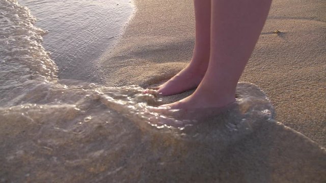 Feet in Water Waves on Sandy Beach with Sea Foam on Coast. Young Woman Stood on Seaside Shore in Spanish Seaside..