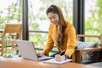 Business Attractive Asian young woman working with laptop smile and writing idea and requirement for success job outside office in coffee shop,Small Business Concept,Warm Tone