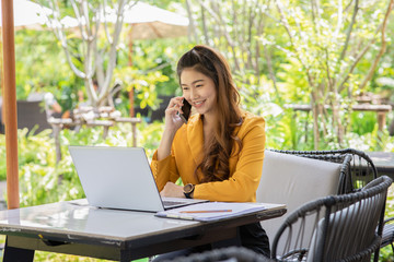 Business Asian young woman working with laptop smile and talking with customer in smartphone to get idea and requirement for success job outside office in coffee shop,Small Business Startup Concept