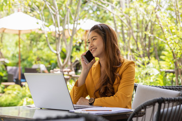 Business Asian young woman working with laptop smile and talking with customer in smartphone to get idea and requirement for success job outside office in coffee shop,Small Business Startup Concept