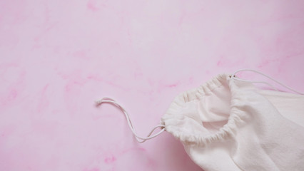 A white draw string cotton pouch with the opening opened, on a pink surface.
