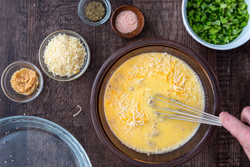 Ingredients for quinoa egg bake, raw egg mix in glass bowl with metal whisk, quinoa, cheese, herbs,...