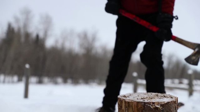 Man chopping wood with an axe during a snowy winter day in slow motion.