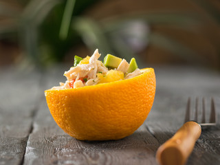 Chicken, avocado and orange salad in half orange and fork on wooden table.