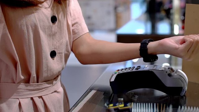 Young Asian woman using smartwatch to purchase product at the point of sale terminal in a retail store with near field communication nfc radio frequency identification payment technology 