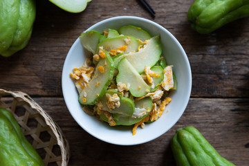 Fresh chayote fruits (Sechium edulis) stir fried with egg and garlic in bowl on wood background
