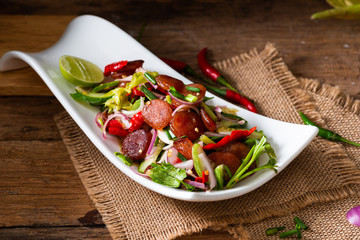 Spicy Chinese pork sausage with vegetable Thai salad in white plate on wood background