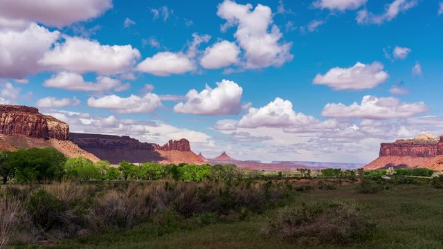 White fluffy clouds float and swell above the craggy mesas and red rocks and red rocks of Southern Utah's Canyon Lands.