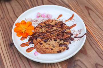 chocolate cookie with caramel on cerabic dish with yellow flower on wooden table