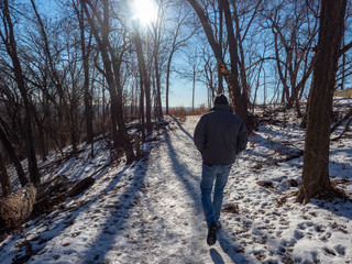 Man walking on snowy trail through forest in winter in Minnesota Valley National Wildlife Refuge, Bloomington , Minnesota, USA