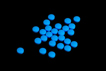 Blue pills are scattered on a black background.