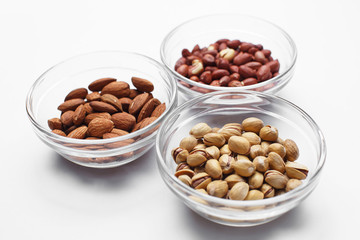 peanuts, almonds and pistachios in bowls on white background