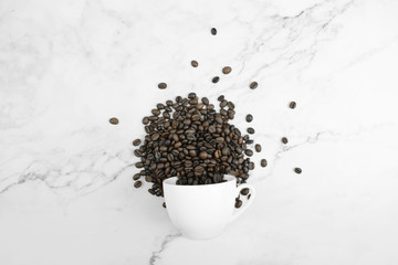 Overturned white glass and coffee beans arranged on a marble pattern in the top view. Isolated background.