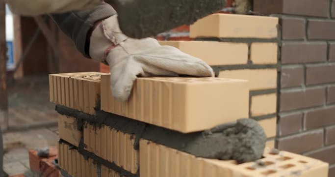 Facing brick is laid in prepared mortar, mason taps with trowel, adjusts masonry level, takes out level for inspection, puts it on masonry, taps on brick, construction work, building construction
