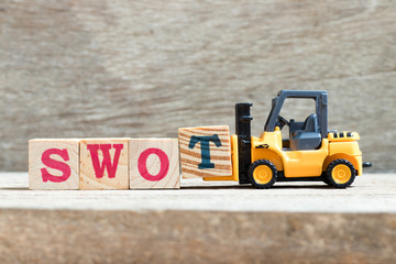 Toy forklift hold letter block T to complete word swot (abbreviation of strength, weakness, opportunities, threats) on wood background