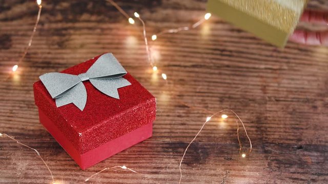 hand placing a second Christmas gift box next to another surrounded by festive golden fairy lights
