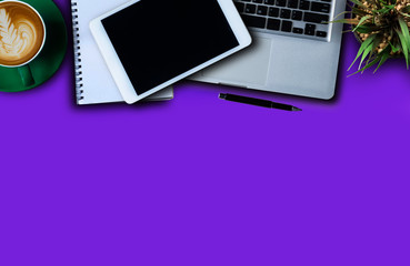 Office supplies are tablet, pen, computer, notebook, mobile phone and red coffee mug placed at an office desk and have a Blue violet background.