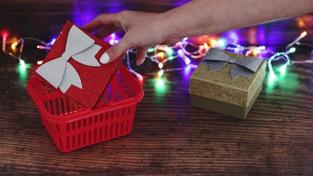 hand moving festive Christmas gift boxes into shopping basket surrounded by fairy lights