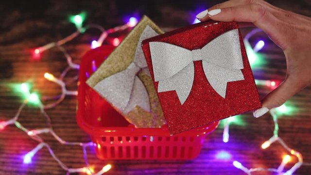 hand grabbing one festive Christmas gift box after the other from inside shopping basket surrounded by fairy lights