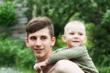 A teenager with a child in her arms, against the background of the summer landscape.